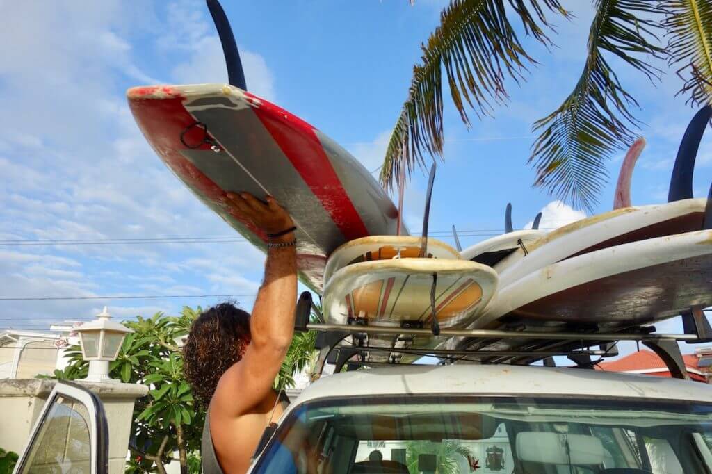 Bodie loads surfboards onto a white van while preparing for a surfing session, Bodie's school of surf is one of the best Barbados Surf Schools