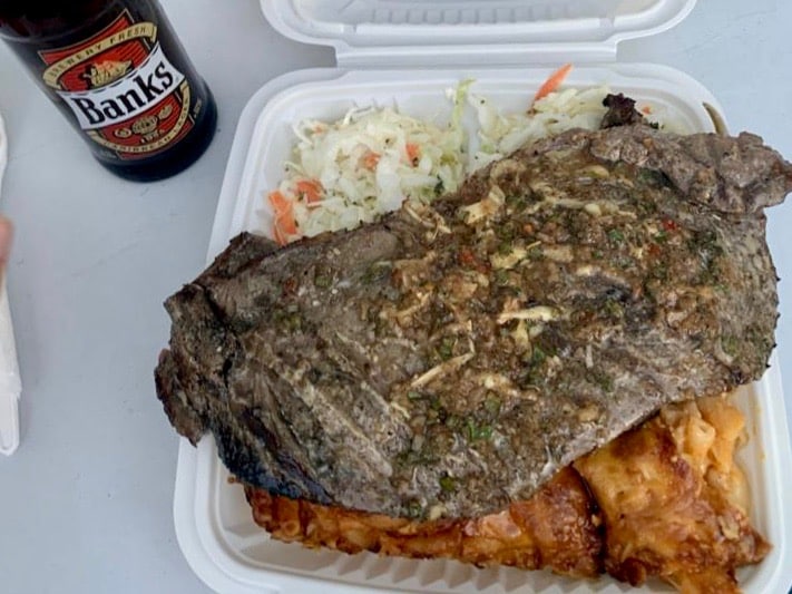 A grilled fish plate from the Oistins Fish Fry. There's a large piece of grilled fish on top of coleslaw and macaroni pie