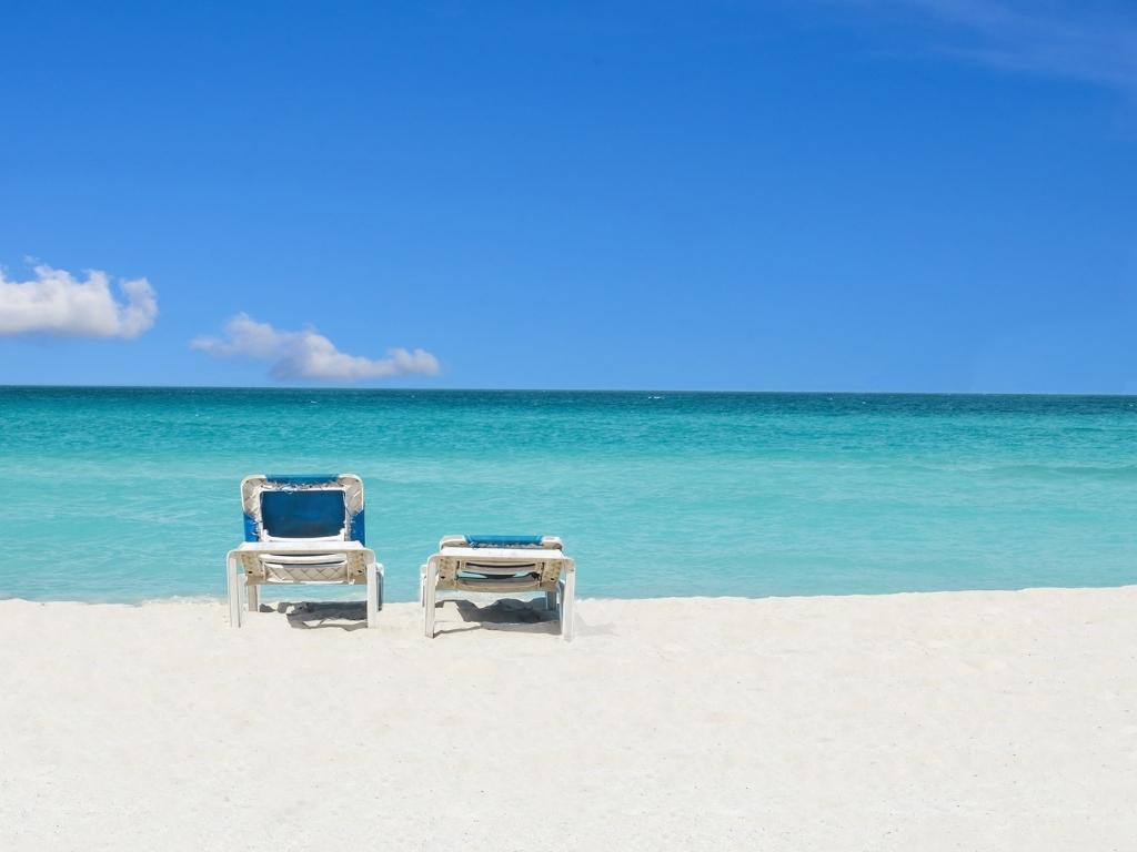 Two sun loungers on a white sand beach facing the blue ocean