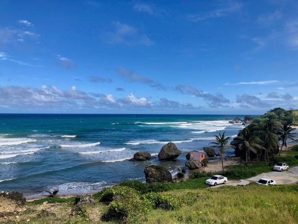 A coastal view of Bathsheba, one of the best Caribbean surfing destinations. There's a pink structure on a rock and a few cars parked along the road