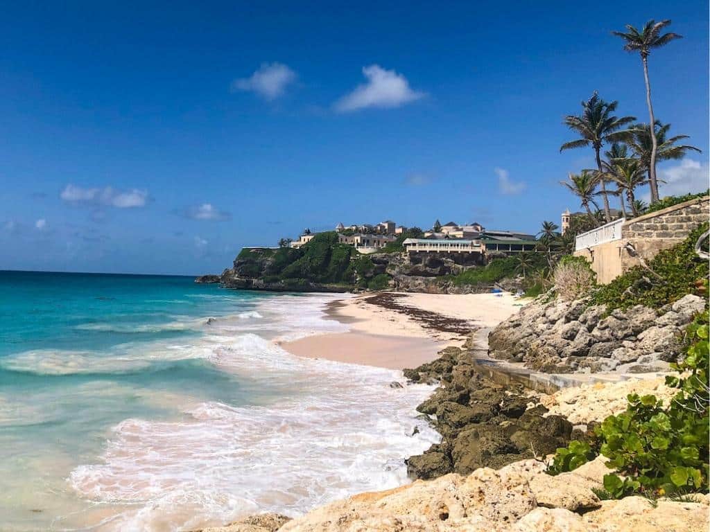 The Crane Beach is a pink sand beach in Barbados. You can see the pink sand in the foreground and the Crane Resort in the background