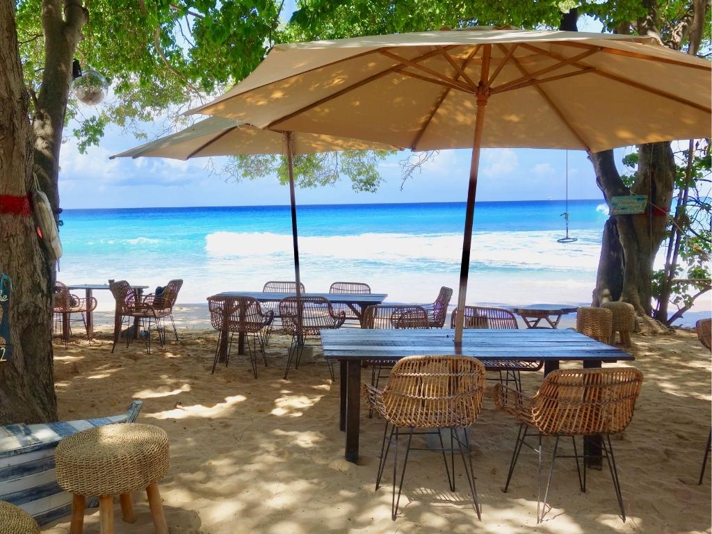 Tables with wicker chairs and large umbrellas on the beach at La Cabane, one of the best restaurants in Bridgetown Barbados