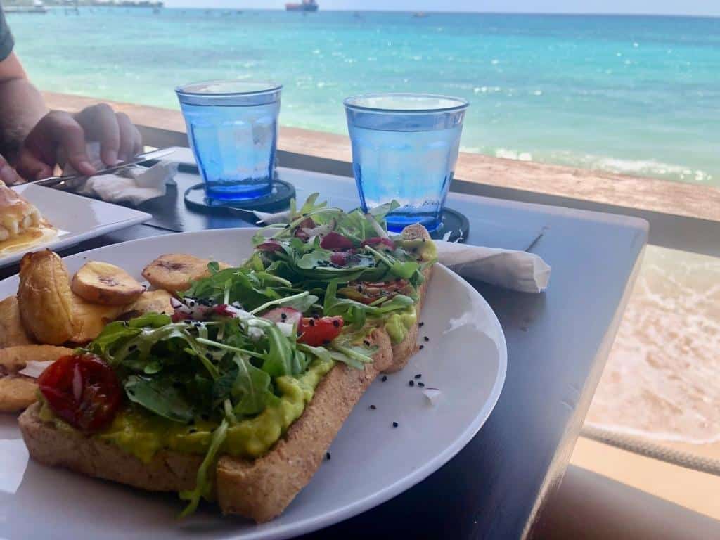 Avocado toast with salad and a side of plantains at Surfers Cafe in Barbados. The ocean is visible in the background.