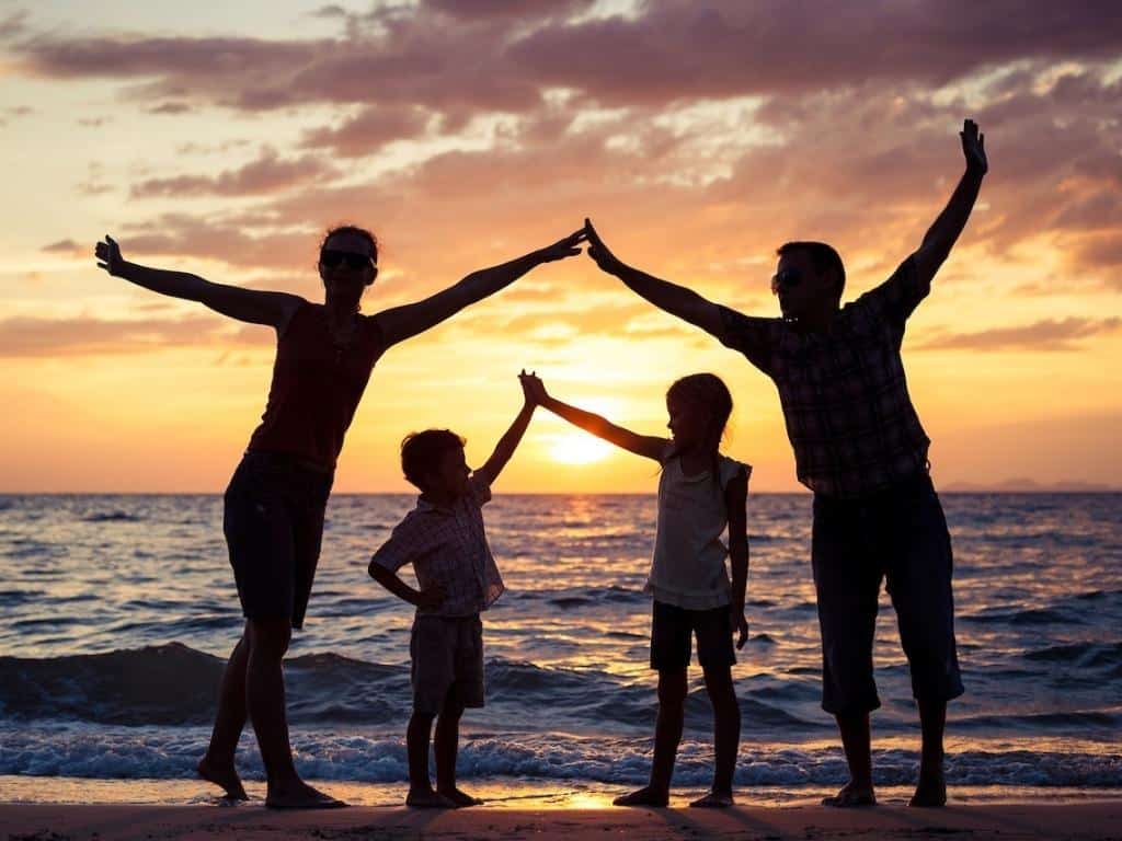A family standing on the beach at sunset holding hands