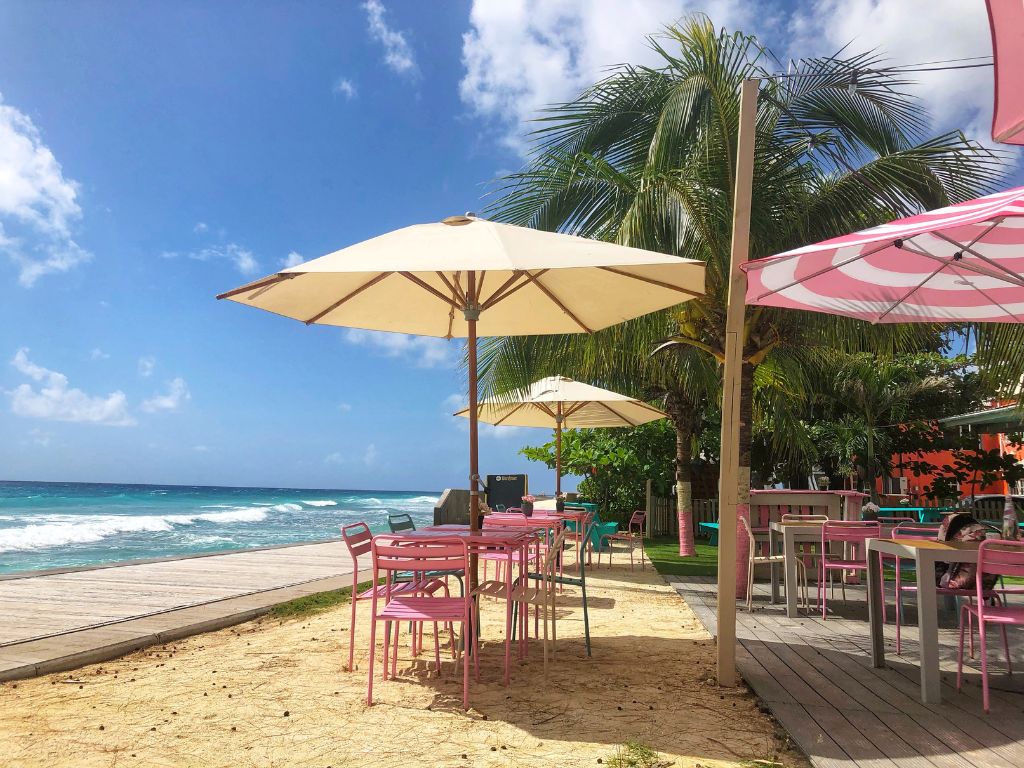 White and pink striped umbrellas over pink tables with a sea view at Baby Doll Restaurant Barbados
