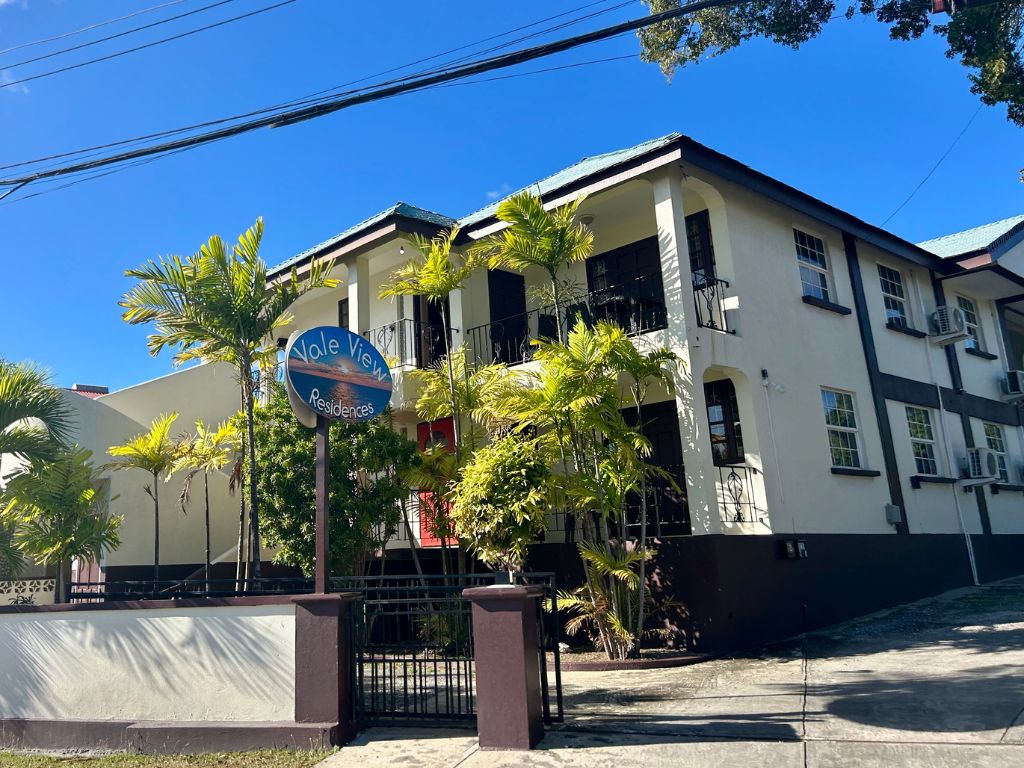 The exterior view of Red Door Condos. The white building is surrounded by palm trees and the units each have a red door